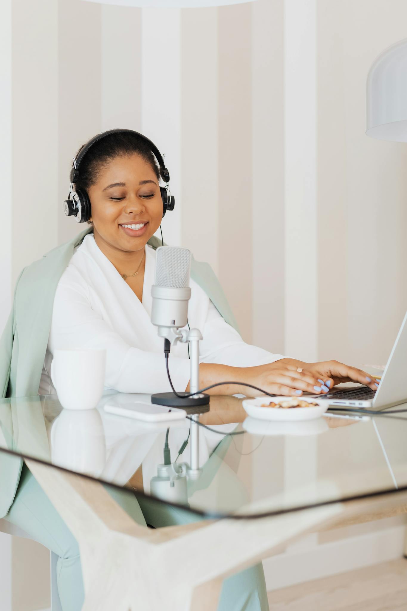 Smiling woman in a white blouse recording a podcast with laptop and microphone.